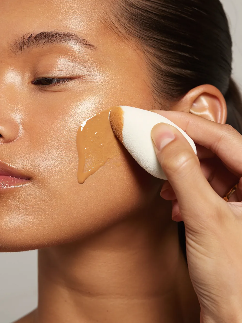 Visagistin trägt Foundation mit einem feuchten Beauty-Blender-Schwämmchen auf trockene Haut auf